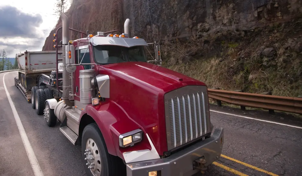 Red diesel truck traveling on a paved road during suspension service conditions