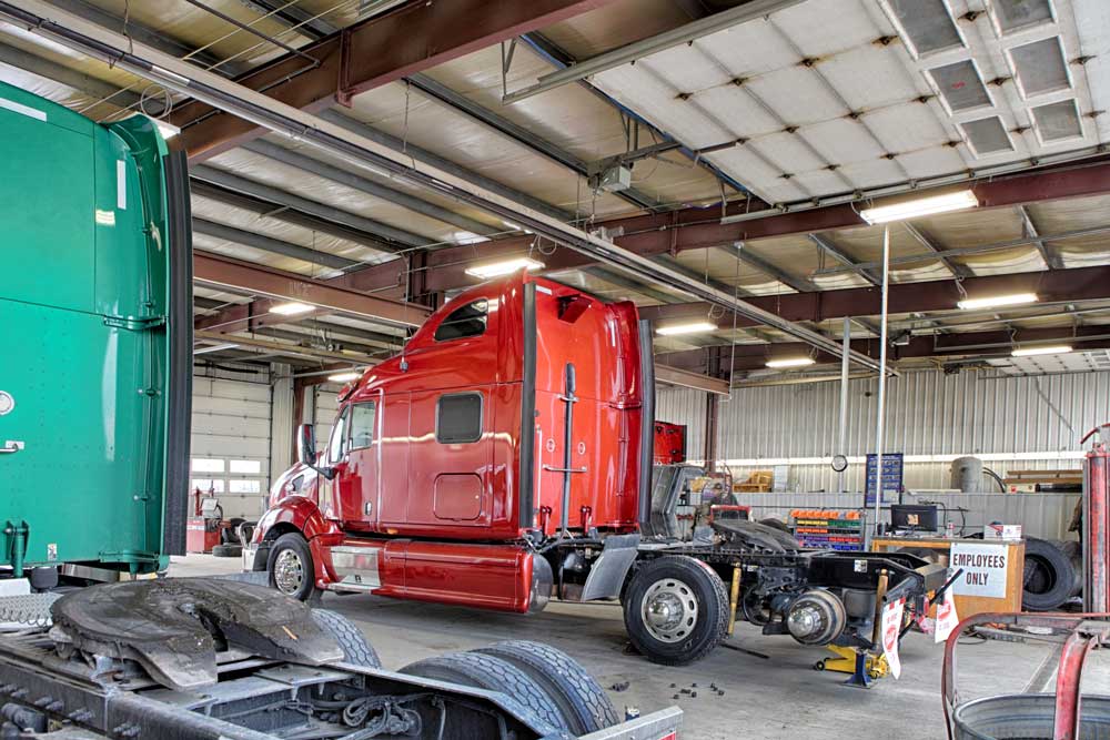 Red and green commercial trucks undergoing suspension repair inside a professional truck service shop