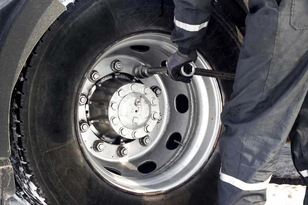 Technician in blue safety clothing servicing a truck tire for balancing